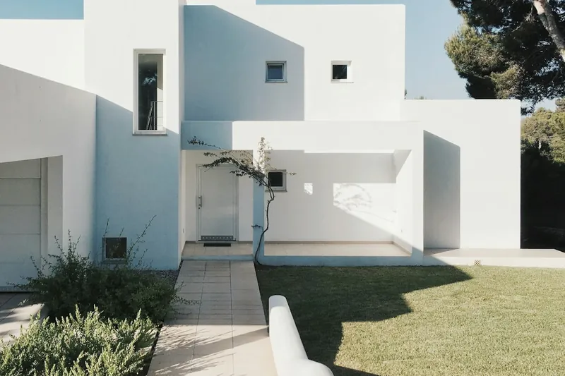Low white boundary wall dividing a lawn from a paved path beside a white stucco house.