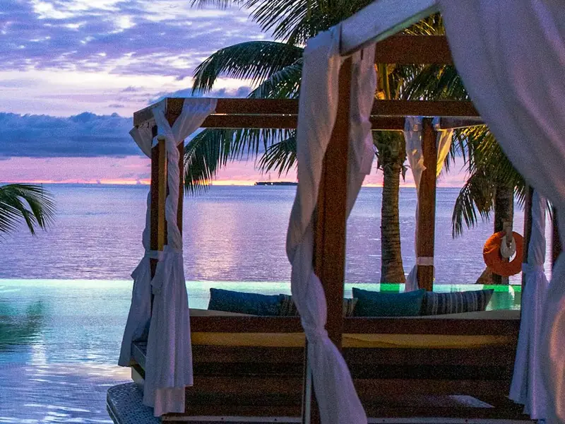 Timber posts and beams with light fabric drapes tied back beside a pool.