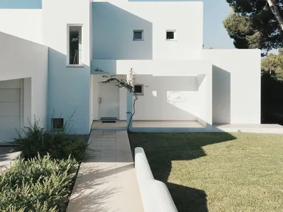 A paved path running between planting and a low white wall, meeting a level lawn beside a white rendered house.