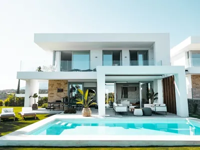 A rectangular pool set into a paved terrace in front of a white two-storey house with deep covered openings.