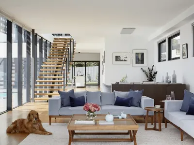 An interior seating area beside a full-height glazed wall, with a staircase behind and a pool visible outside.