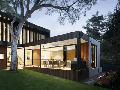A decked terrace and steps along the glazed side of a dark-clad house at dusk.
