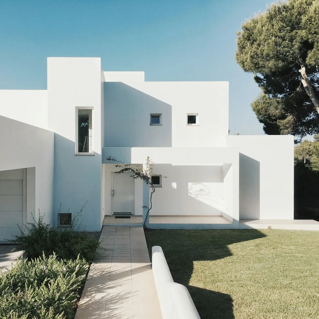 Bright white stucco exterior with stone steps and a paved path under a clear sky.