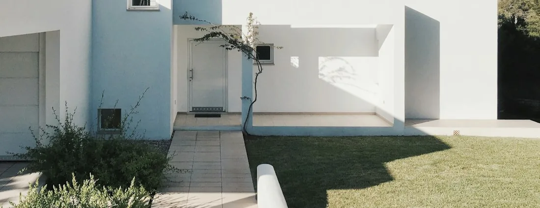 Garage door and a large-format paved approach running past planting to a white rendered house.