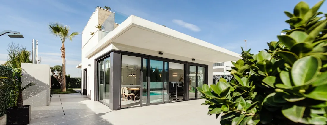 Large-format pale paving running the length of a pool beside a single-storey house.